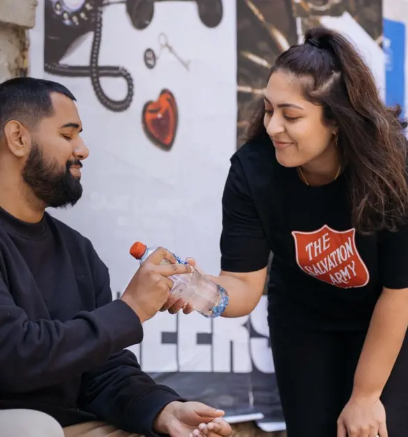 Salvation Army volunteer giving man bottled water.