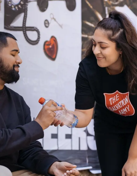 Salvation Army volunteer giving man bottled water.
