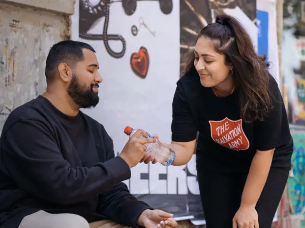 Salvation Army volunteer giving man bottled water.