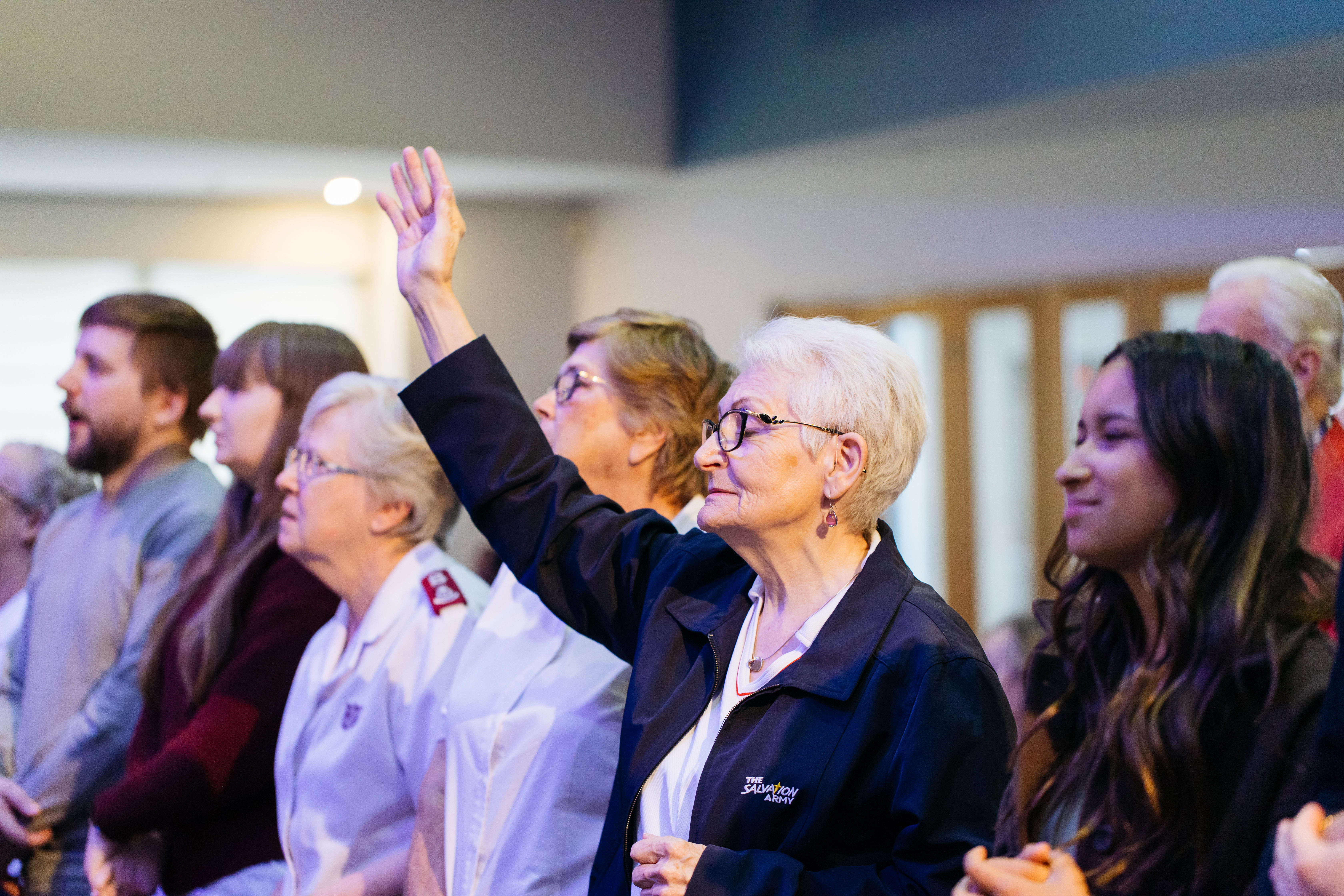 A woman holds a hand to the sky as people gather together during a church service.