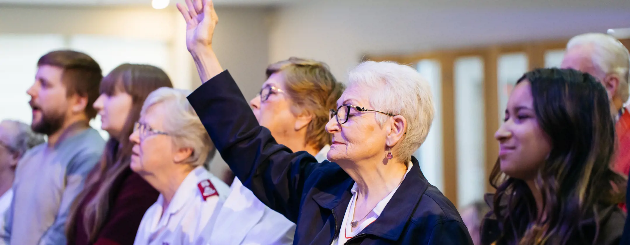 A woman holds a hand to the sky as people gather together during a church service.