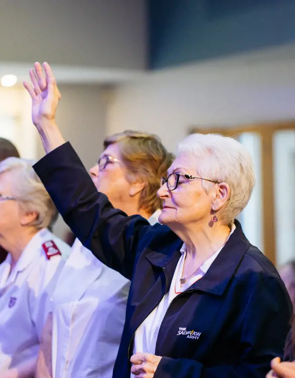 A woman holds a hand to the sky as people gather together during a church service.