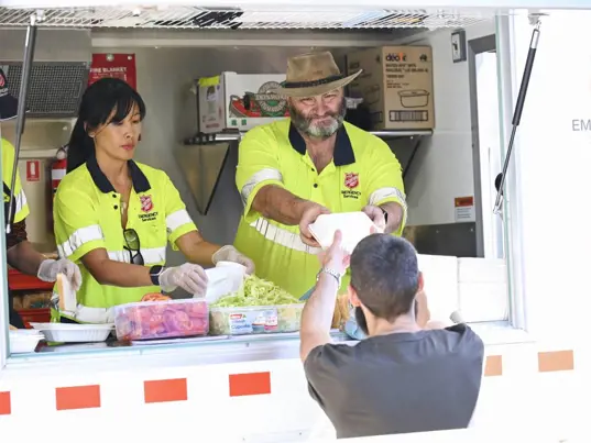 Two Salvation Army Emergency Services workers serve food and drink from the Food Truck window