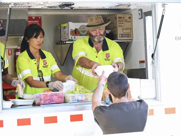 Two Salvation Army Emergency Services workers serve food and drink from the Food Truck window
