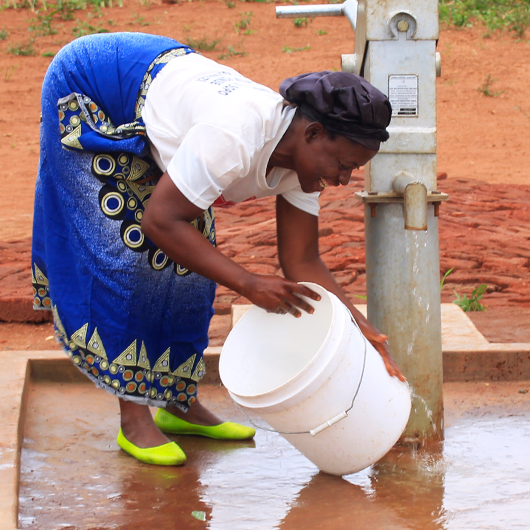 Woman bending over beside borehole pump with bucket
