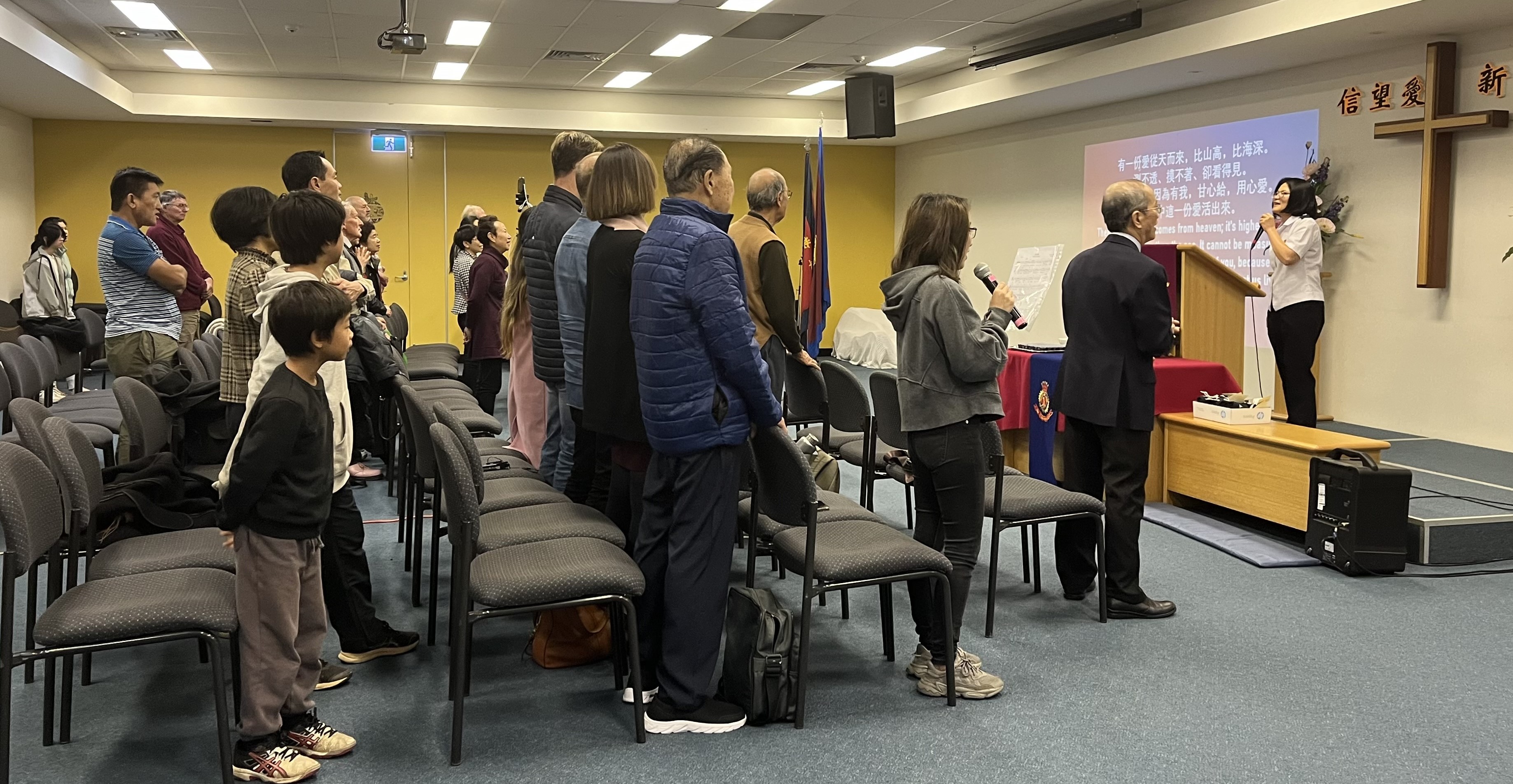 People standing in worship while listening to the Corps Officer at the front of the worship hall.