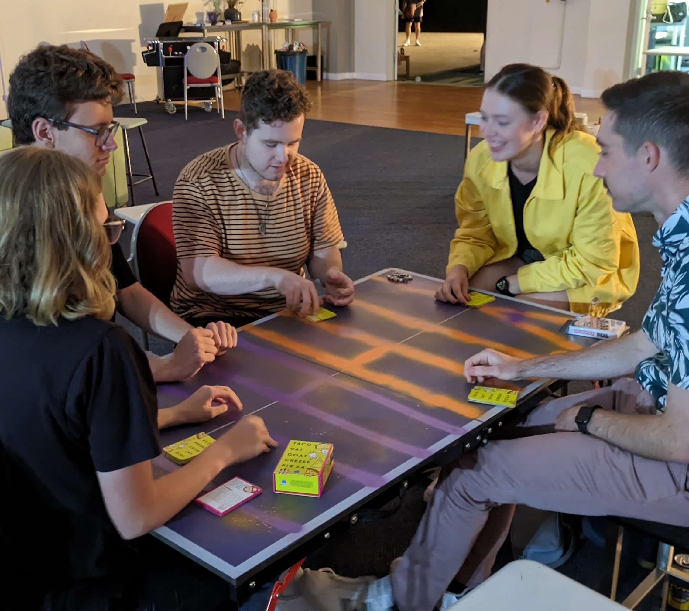 A group of young adults sitting around a table and playing a card game.