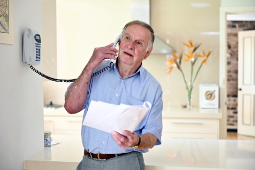 Man speaking on the phone while reviewing funeral paperwork at home