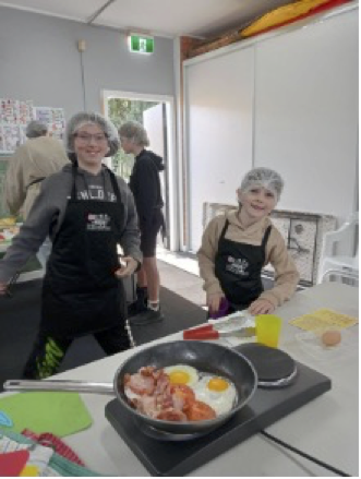 Two children at an event, cooking breakfast. 