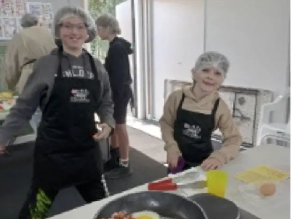 Two children at an event, cooking breakfast.