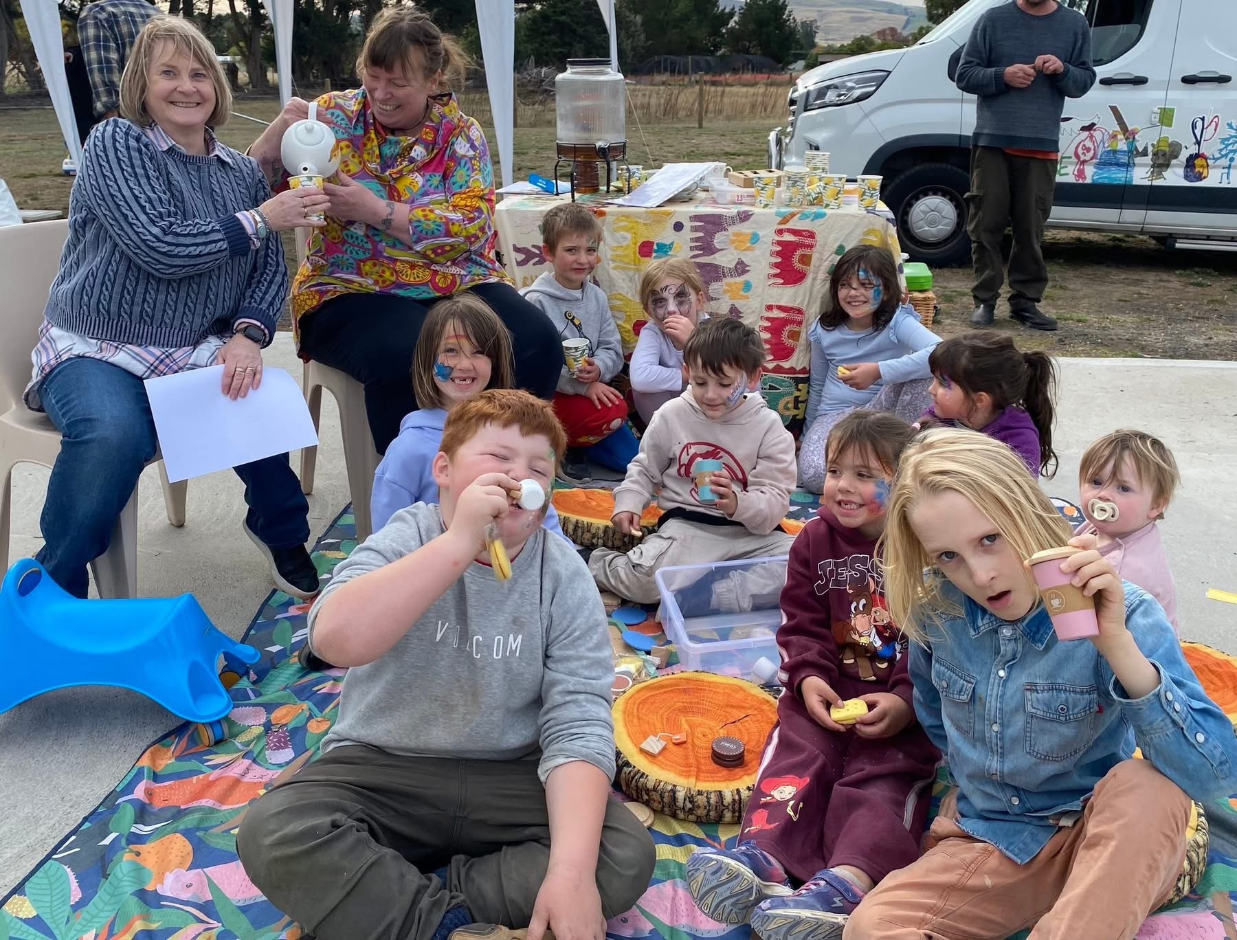 The travelling tea party - kids smiling while sitting on a mat outdoors