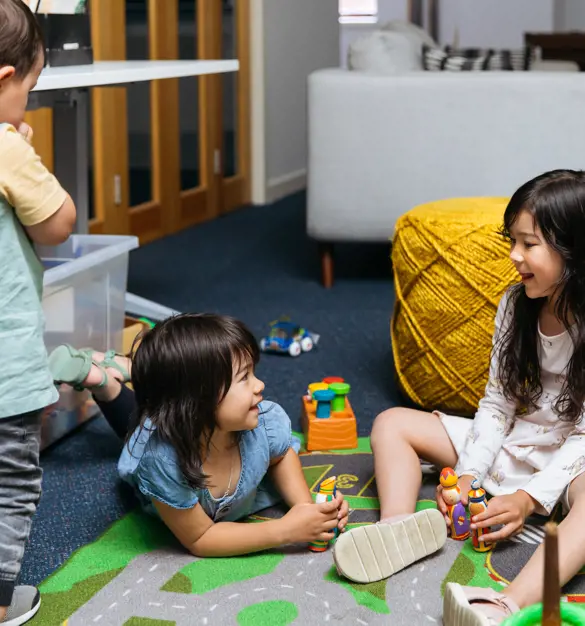 Three children similing as they play on a playmat.