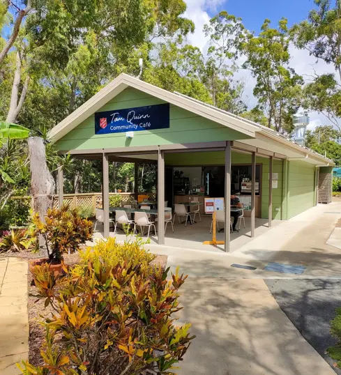 The Tom Quinn Community Cafe - a light green, pitch-roofed cabin with a shaded outdoor area